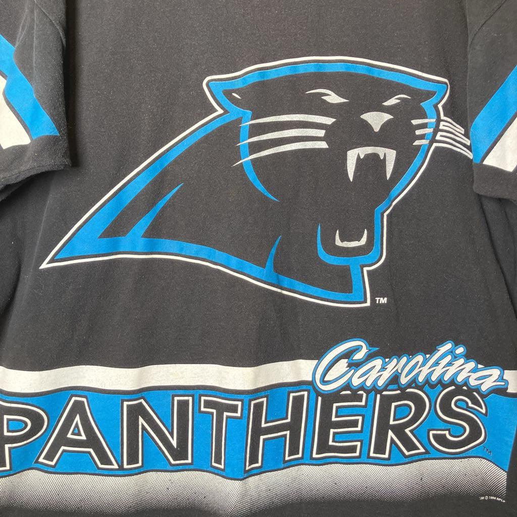 A close-up of a Carolina Panthers graphic t-shirt featuring the team's panther logo in black and blue with white outlines, and 'Carolina PANTHERS' text across the bottom.