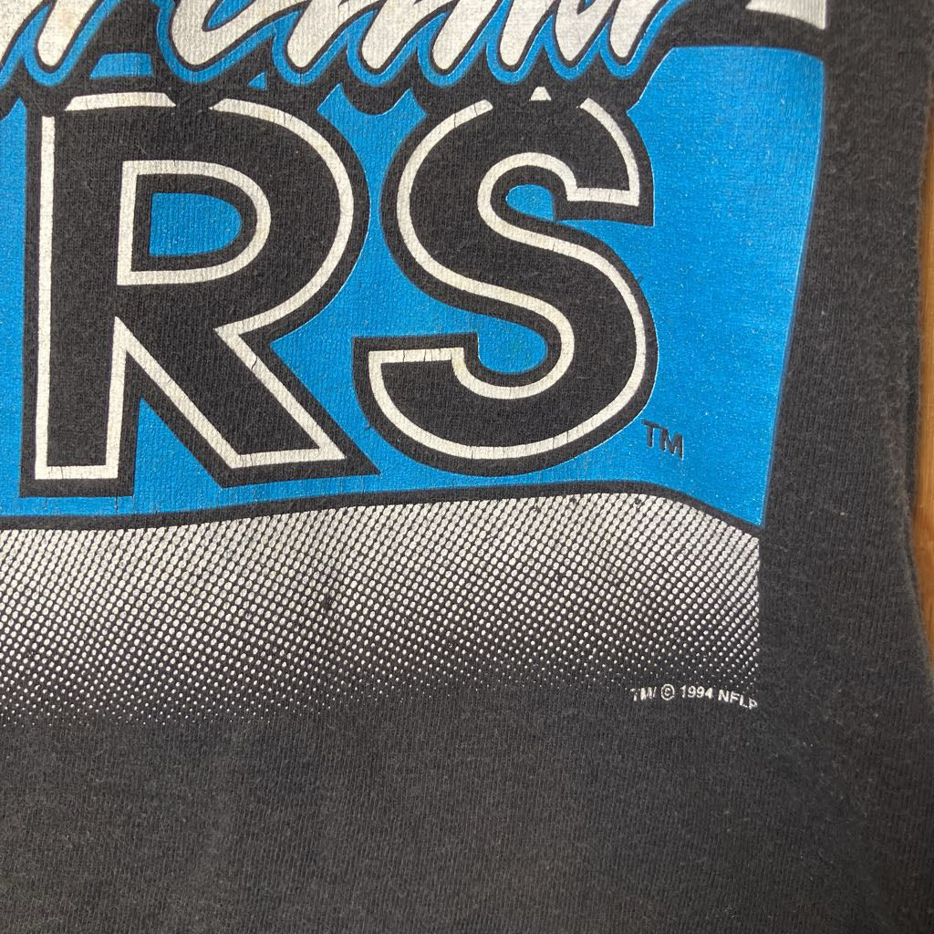 Close-up of a vintage black graphic t-shirt featuring a bright blue panel with bold white and black lettering and a gray halftone pattern.
