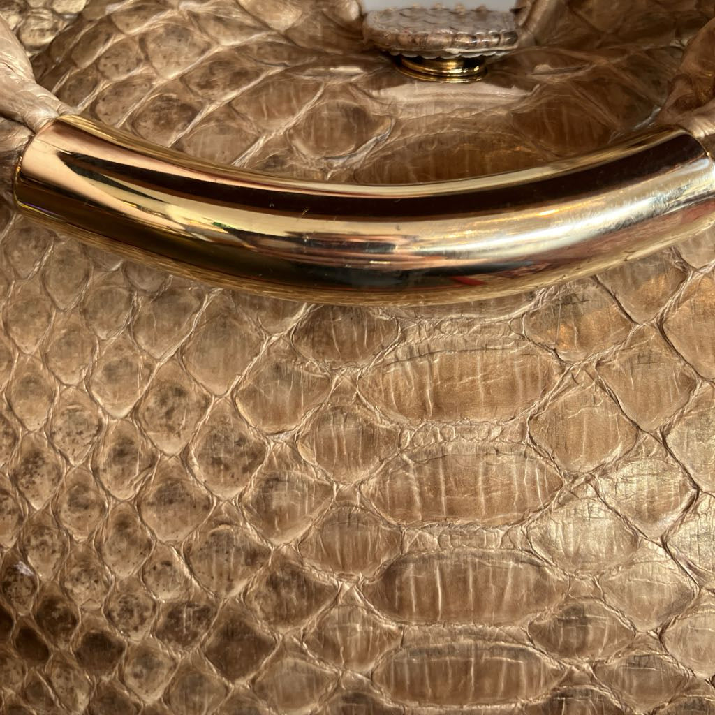 Close-up of a metallic gold handle attached to a champagne-gold textured crocodile-patterned bag.
