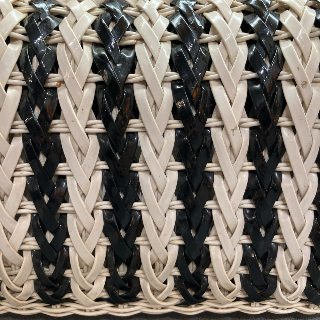 Close-up of a woven basket or bag featuring alternating vertical stripes of glossy black and warm off-white plastic or resin strips.