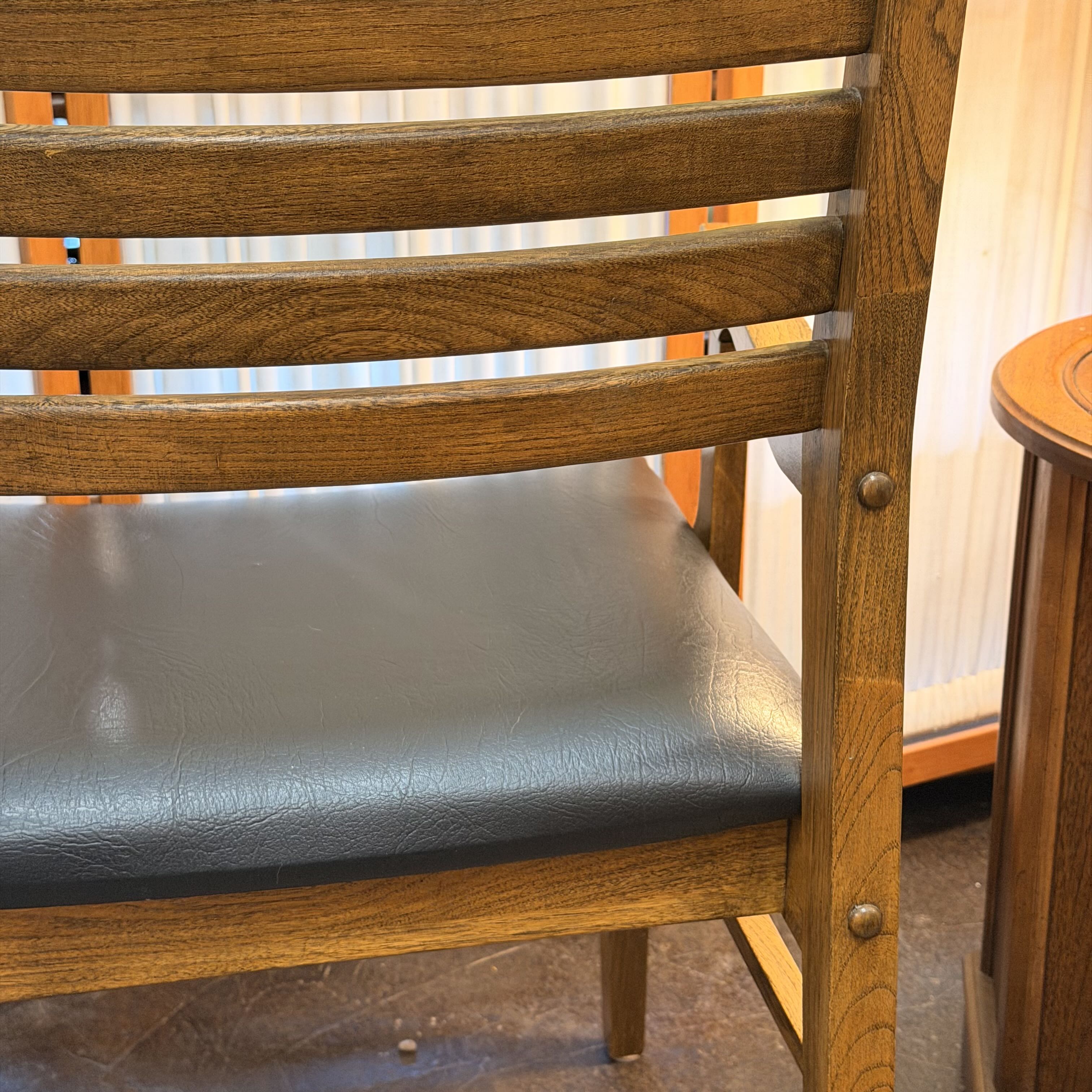 Close-up of a wooden dining chair with a dark gray upholstered seat cushion, showing the slatted backrest and wood grain.