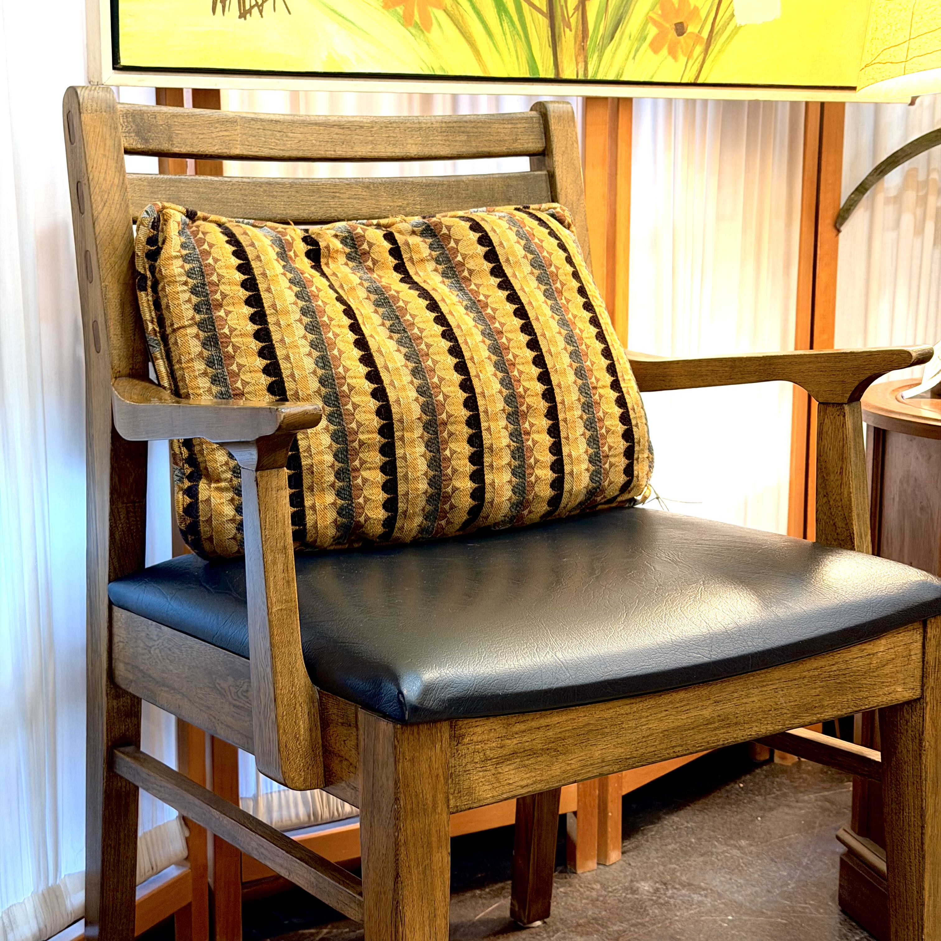 A wooden armchair with a black upholstered seat cushion and a striped throw pillow in yellow, brown, and black, shown in a home interior setting.