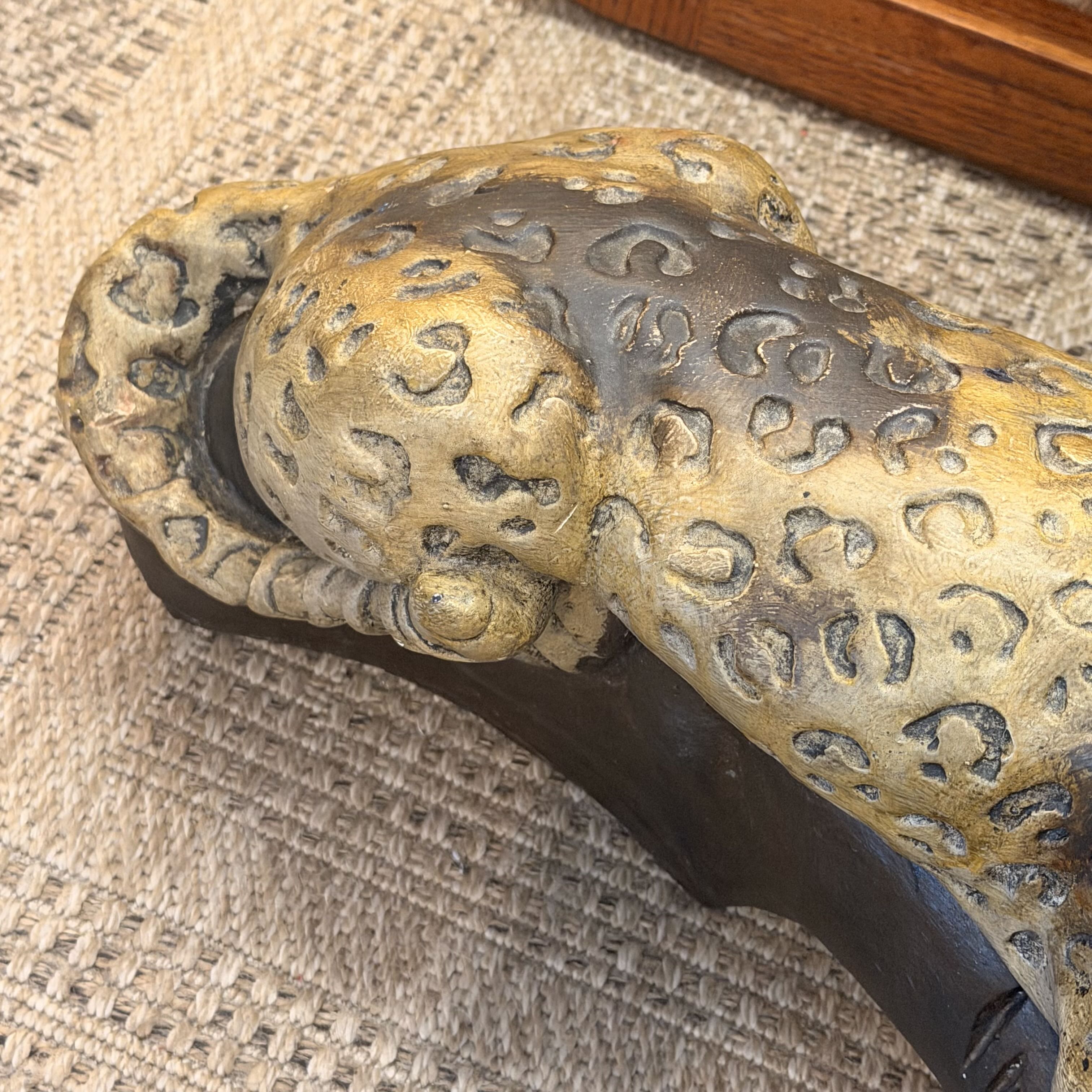 A close-up of a decorative leopard figurine with a textured gold and dark brown spotted pattern, resting on a woven beige surface.