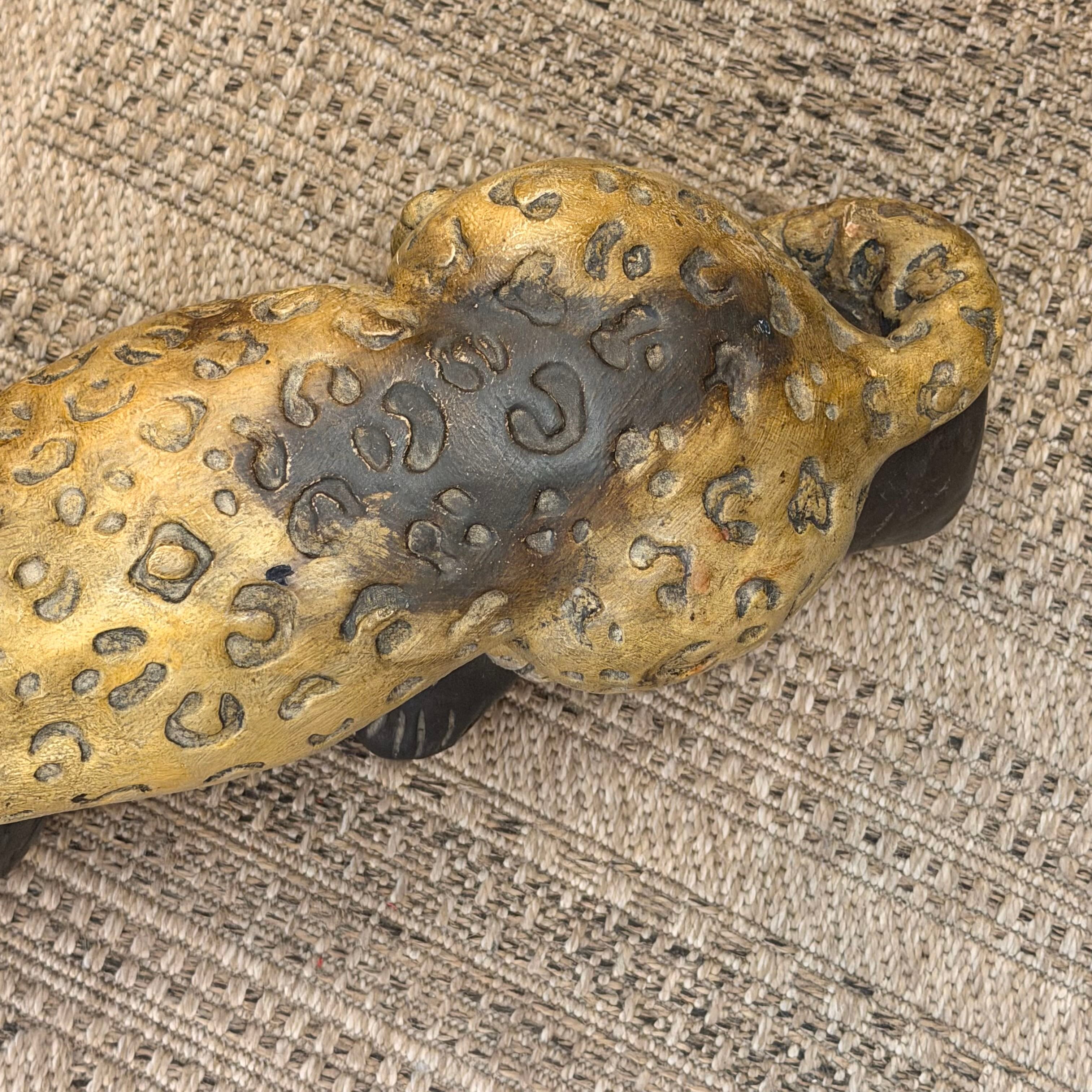 A close-up of a leopard or cheetah figurine with a textured golden-yellow and dark brown spotted pattern, resting on a woven beige fabric surface.