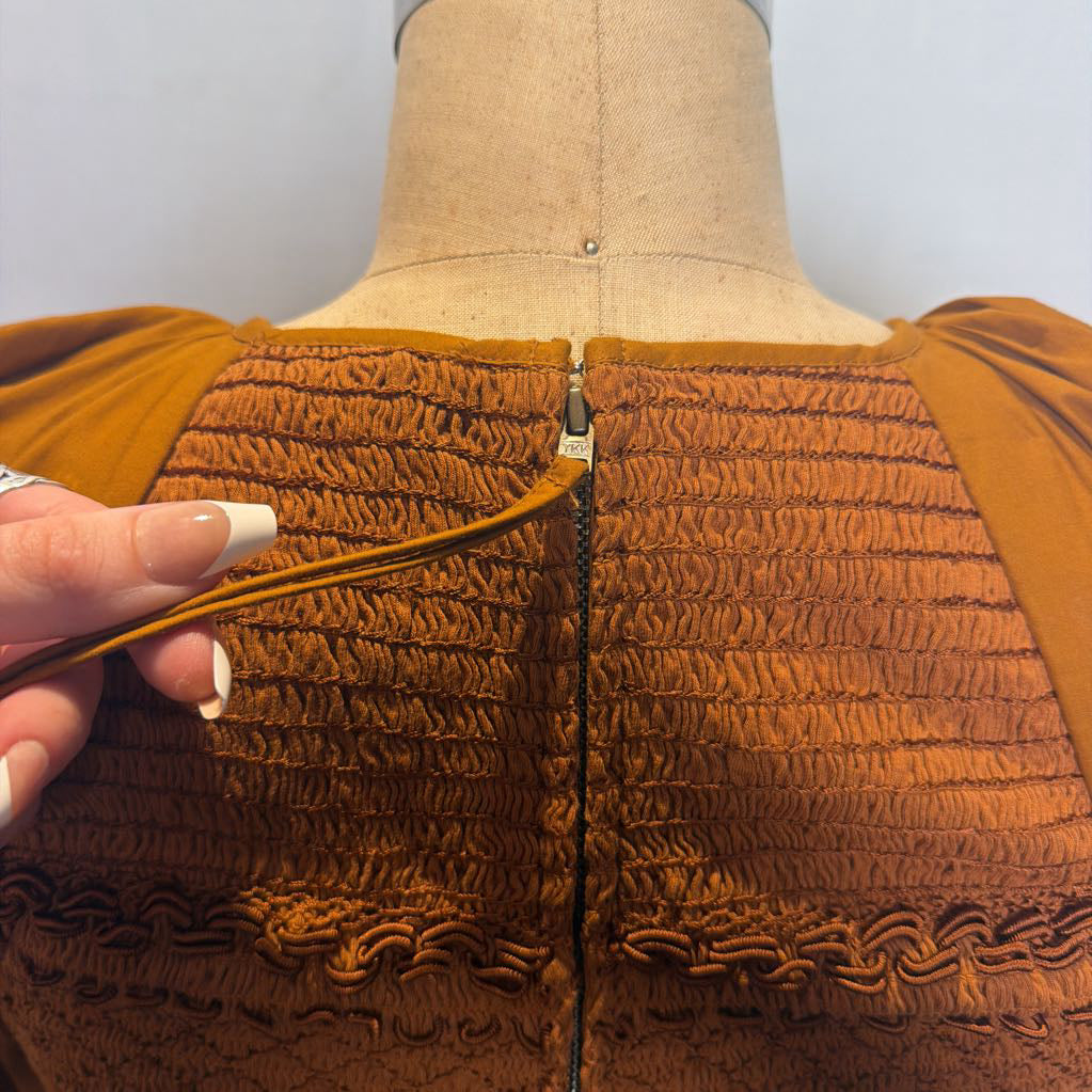 Close-up of a brown smocked fabric garment on a dress form, showing a hand opening a central zipper.