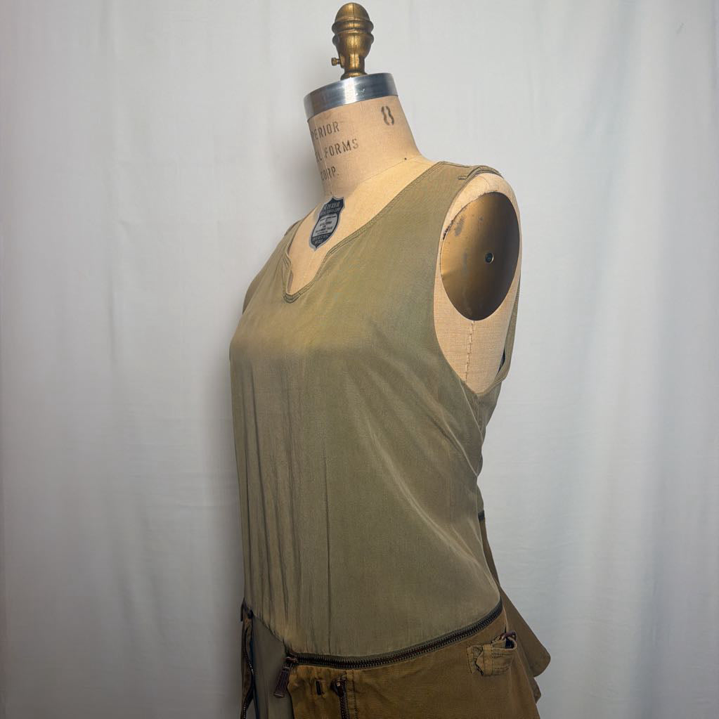 A sleeveless olive green top displayed on a vintage dress form mannequin against a white fabric backdrop.
