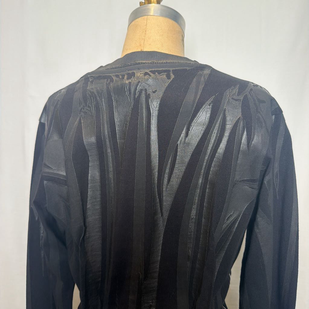 A black long-sleeve top displayed on a dress form, showing a heavily textured, pleated, and crinkled back panel against a plain light background.