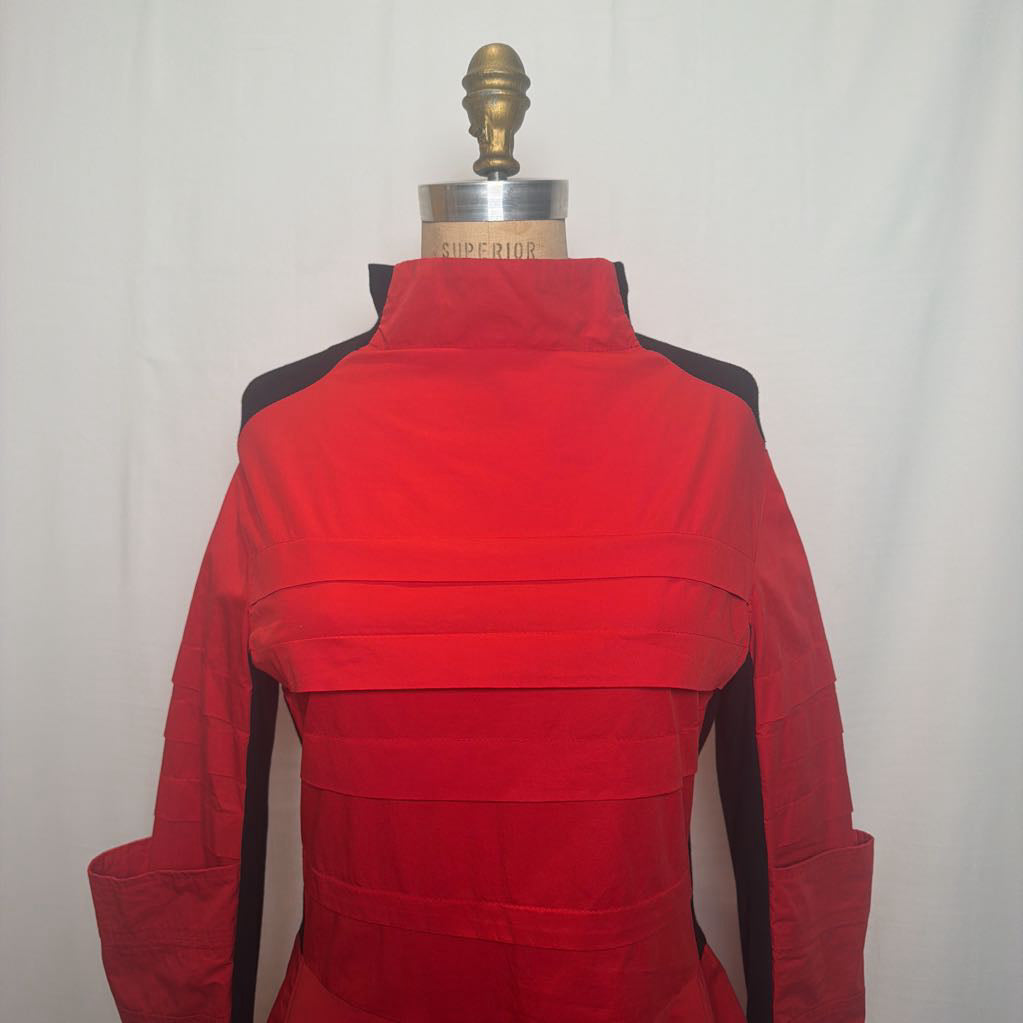 A red long-sleeve jacket or costume top displayed on a dress form mannequin against a white fabric backdrop. The garment has black shoulder yokes and side panels, with a high collar and horizontal seam details across the front.