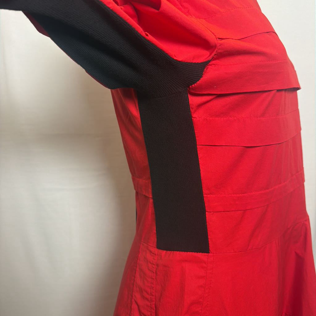 Close-up of a red garment with a black ribbed sleeve and a matching black vertical trim detail, shown against a plain light background.