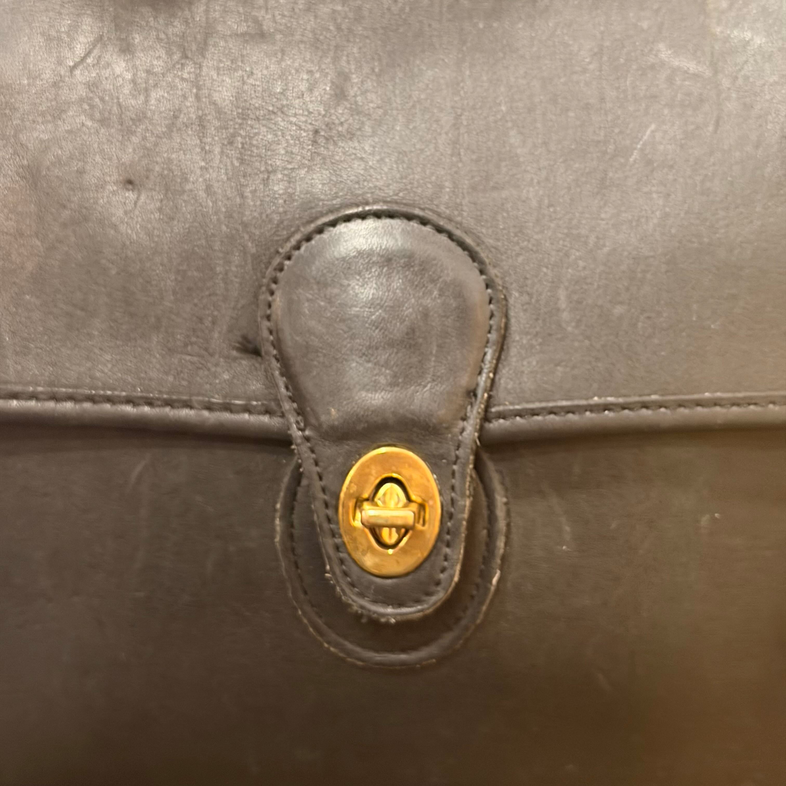 Close-up of a dark brown leather bag featuring a central gold-tone metal clasp and matching leather trim.