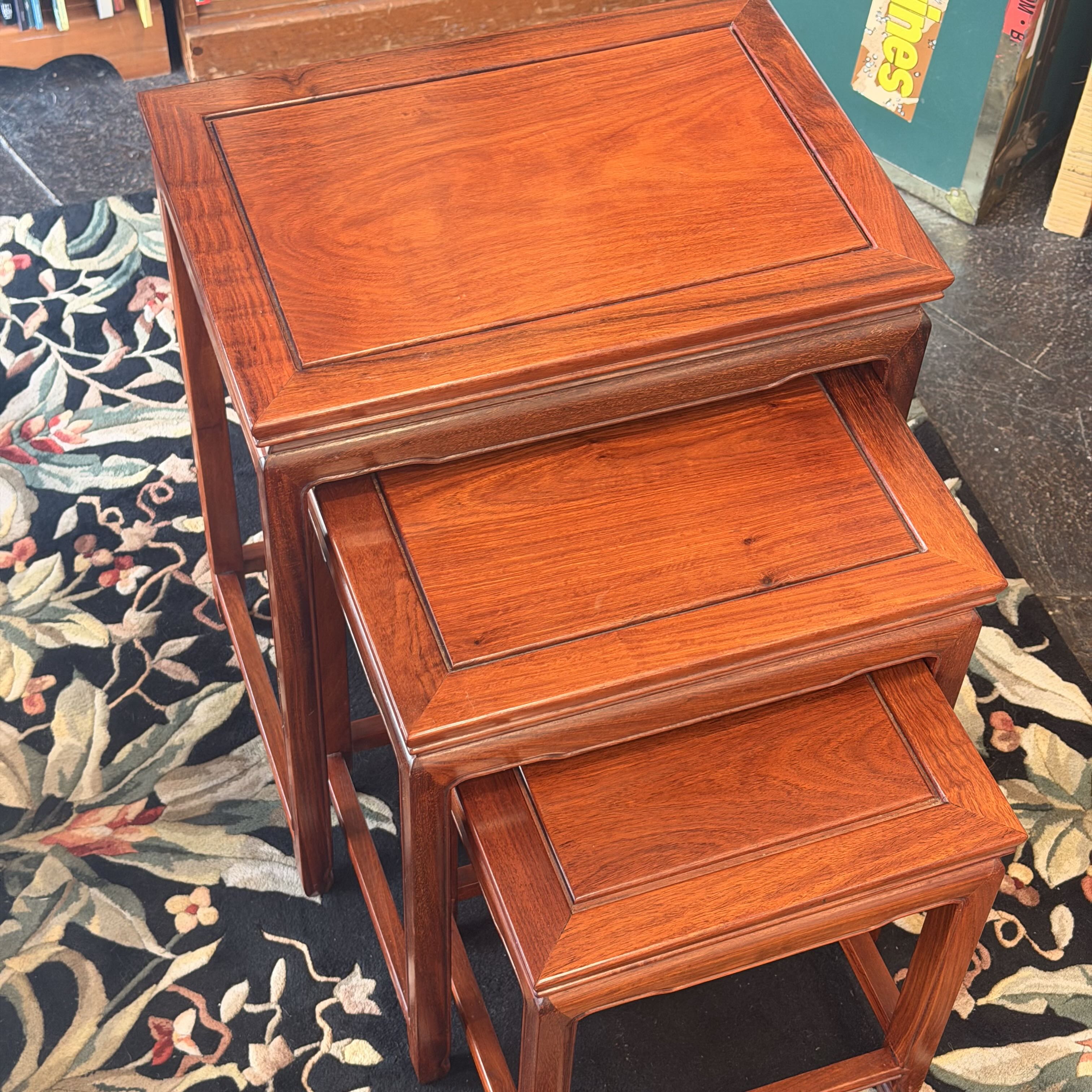 Three nested square wooden nesting tables with a reddish-brown finish and raised panel borders, shown on a floral rug.