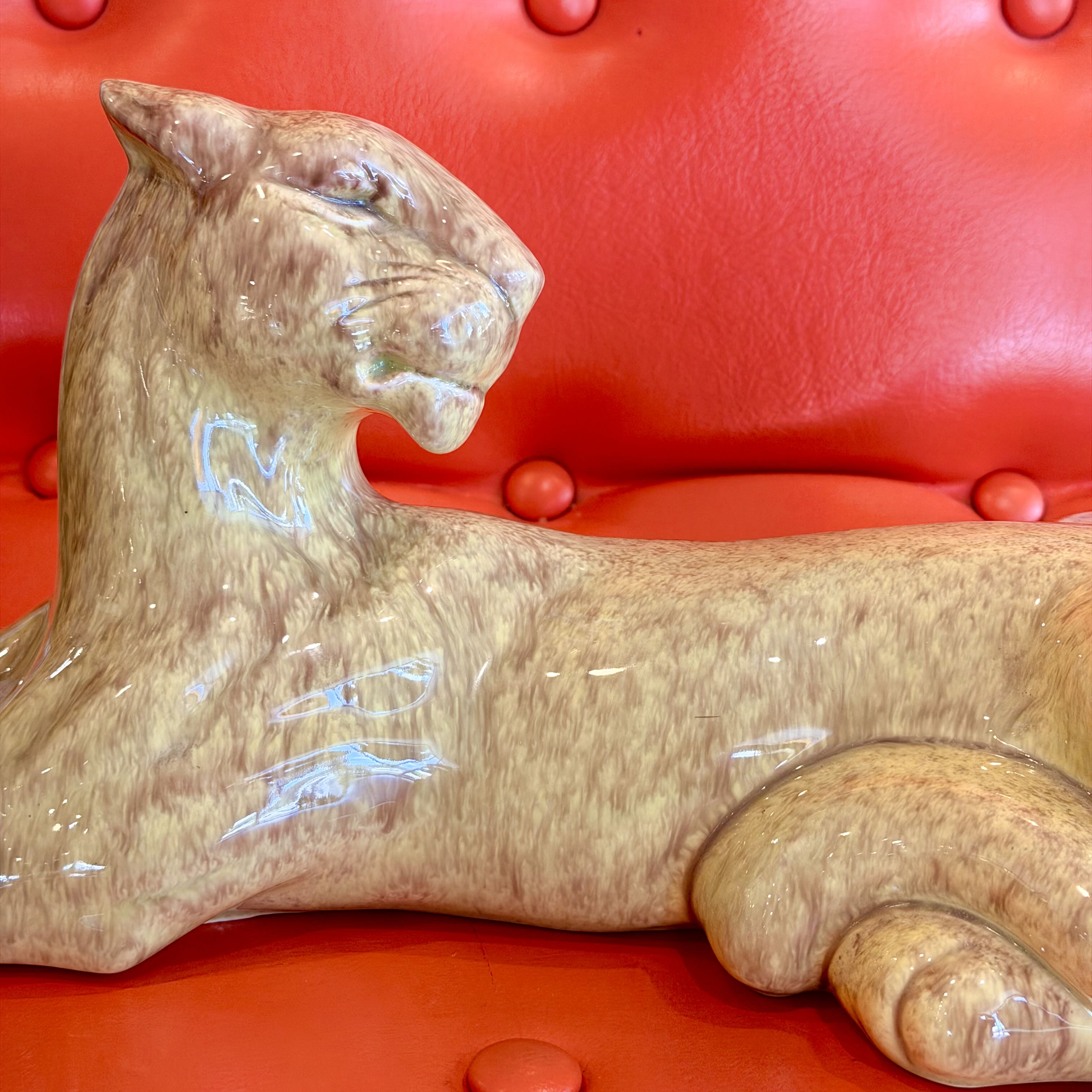 A glossy ceramic panther figurine in a light brown and beige marbled glaze, resting on a vibrant red tufted leather sofa.
