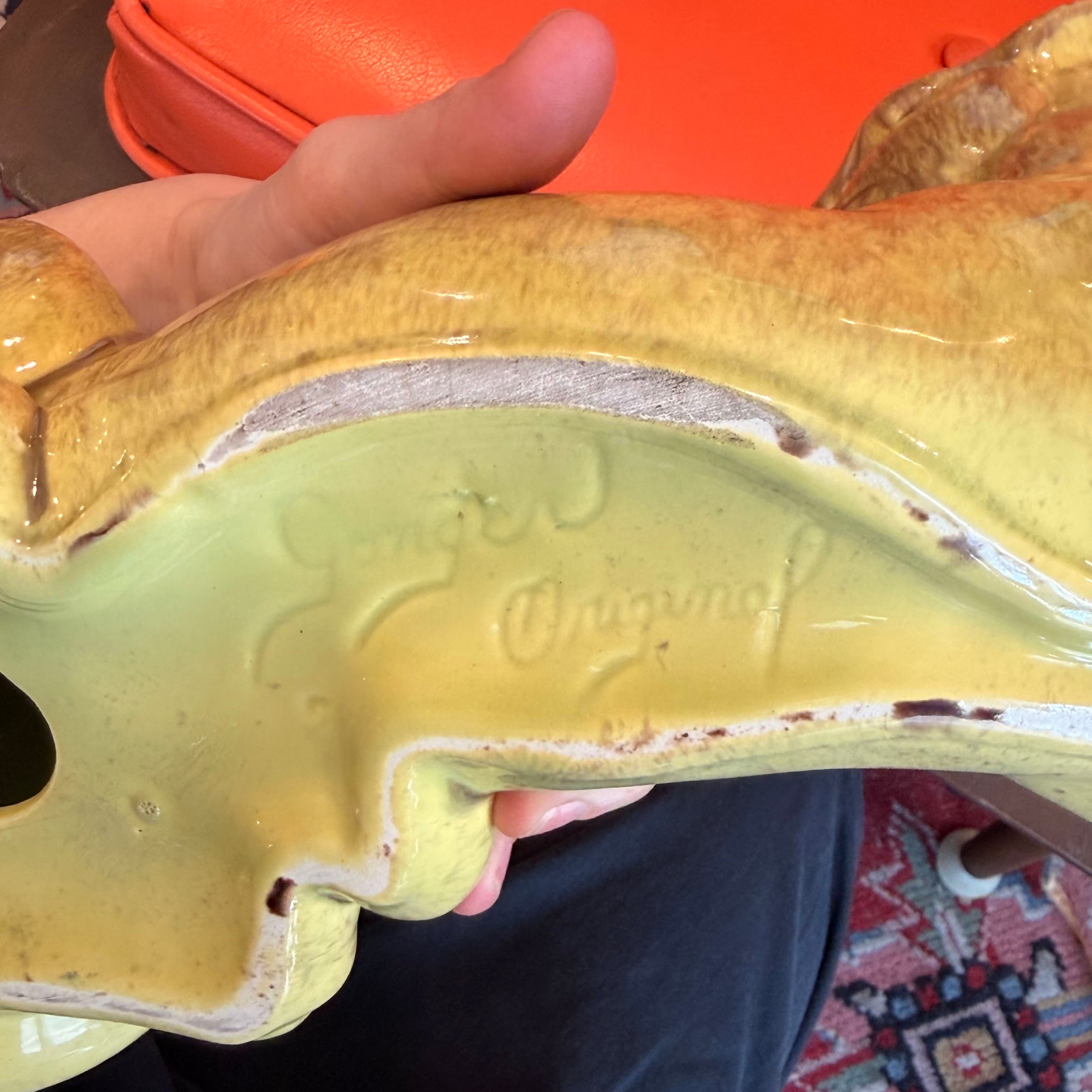 A close-up of a ceramic animal figurine, showing the underside and interior glaze. The figurine has a glossy yellow-green glazed interior and a textured tan-brown glazed exterior.