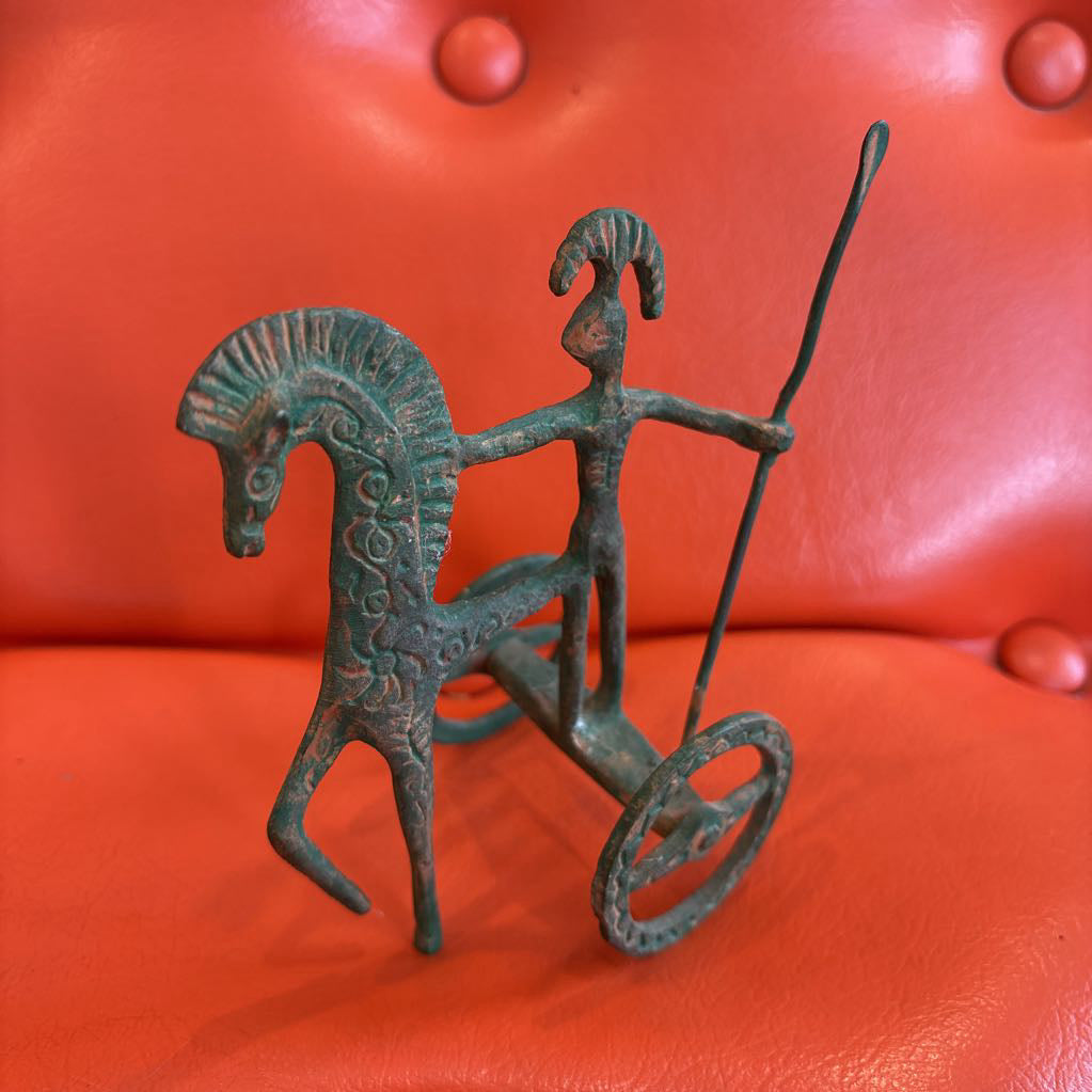 A metal ancient Greek style figure on an orange leather surface.