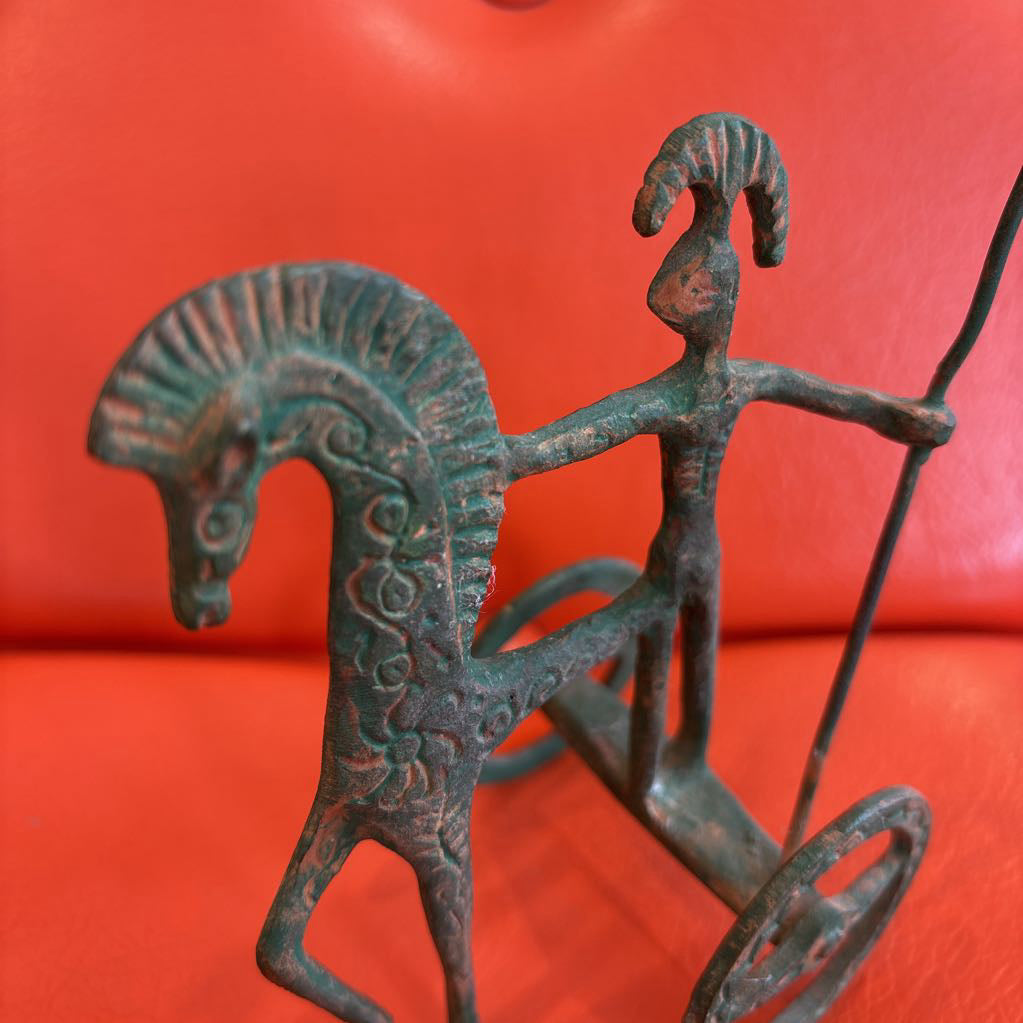 A metal ancient Greek style figure on an orange leather surface.