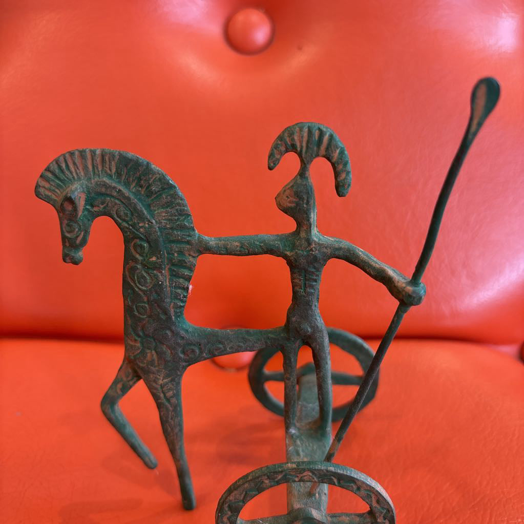 A metal ancient Greek style figure on an orange leather surface.