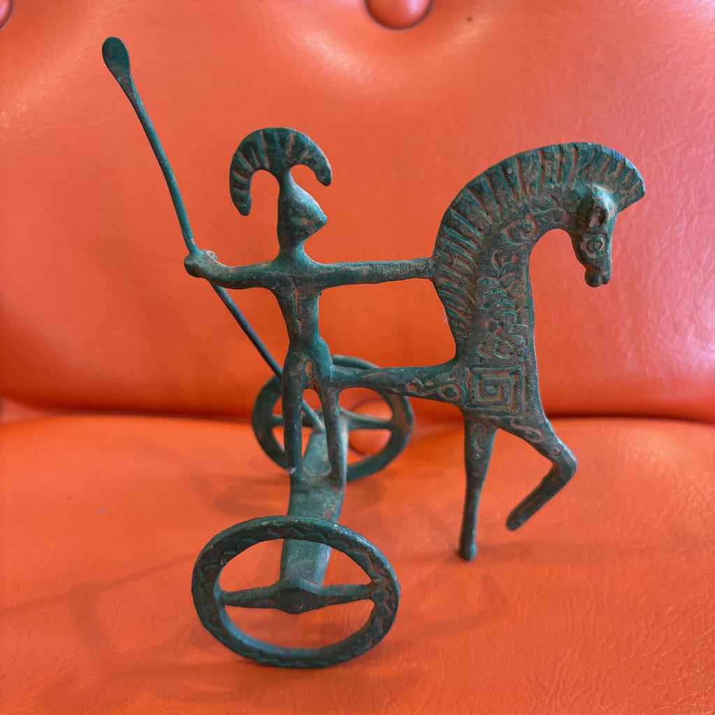 A metal ancient Greek style figure on an orange leather surface.