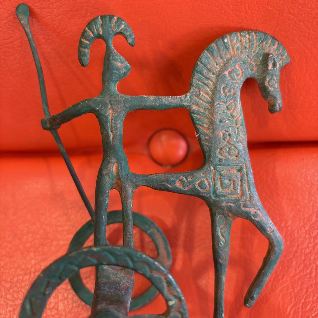 A metal ancient Greek style figure on an orange leather surface.