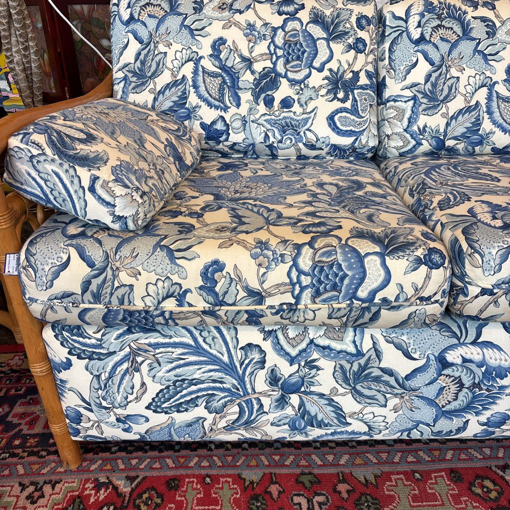A three-seater sofa upholstered in a blue and cream toile-style floral and bird pattern, shown with a wooden frame and a patterned rug underneath.