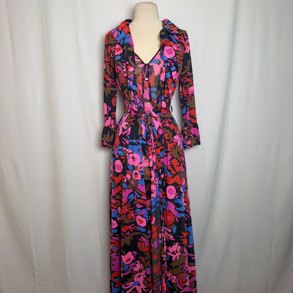 A long-sleeve wrap dress with a vibrant abstract floral pattern in pink, blue, red, and brown on a black background, displayed on a cream dress form against a light gray fabric backdrop.