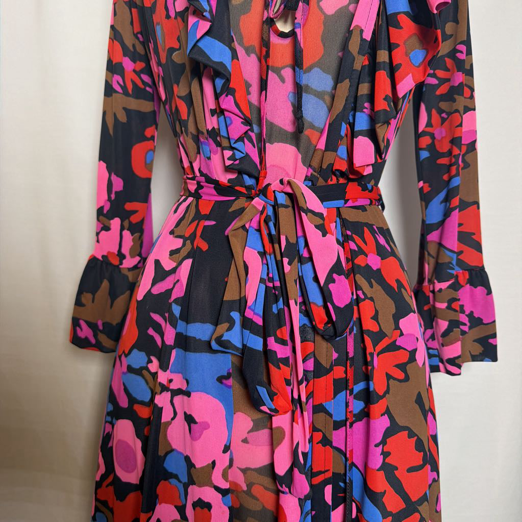 A long-sleeve wrap-style dress with a tie waist, featuring a bold abstract floral pattern in pink, blue, red, and brown over a black base, photographed against a plain light background.