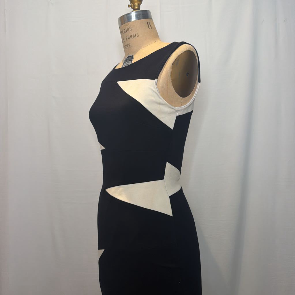 A sleeveless black dress with large white geometric panel accents, displayed on a dress form mannequin against a white fabric backdrop.
