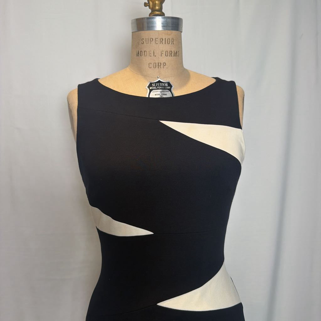 A sleeveless black dress with diagonal cream panels, displayed on a vintage mannequin torso against a white curtain background.
