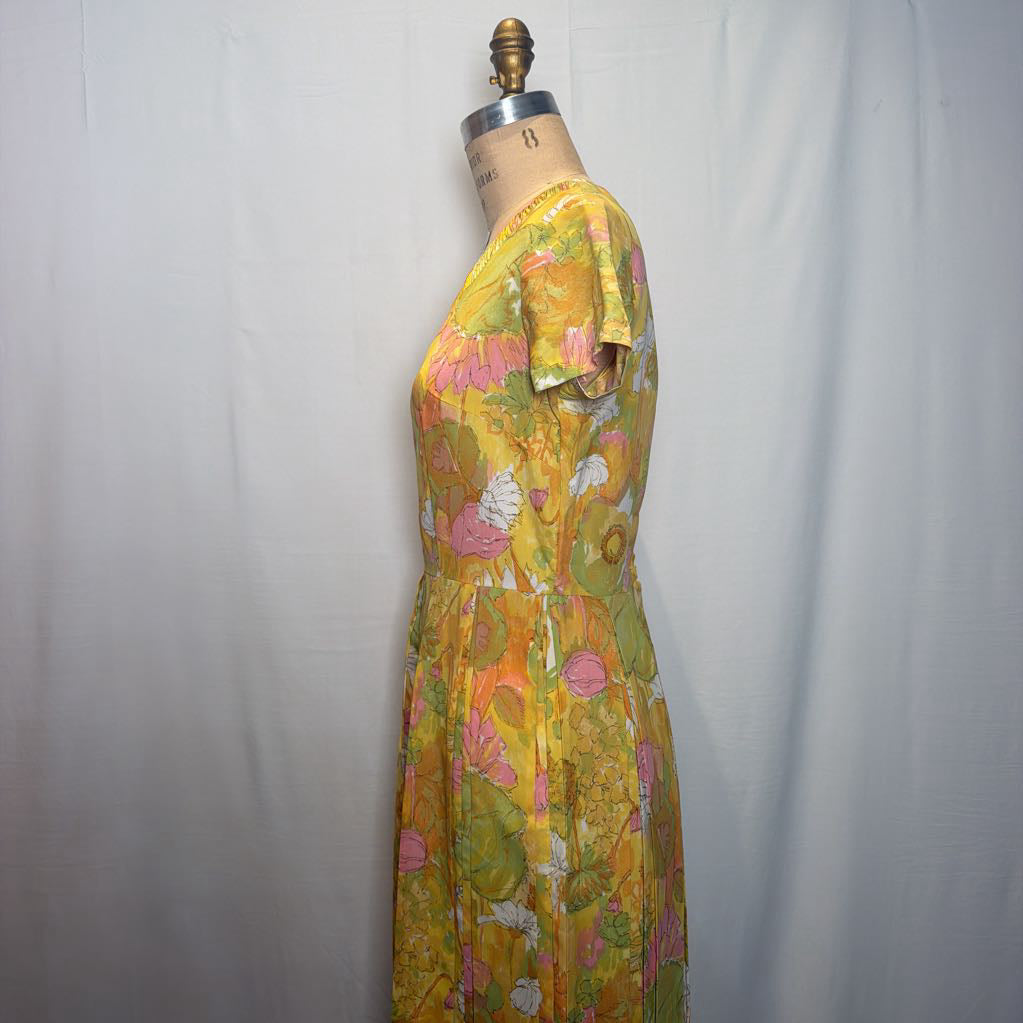 A vintage floral print dress displayed on a dress form mannequin against a white fabric backdrop. The dress features a vibrant yellow base with pink, green, and orange floral patterns.