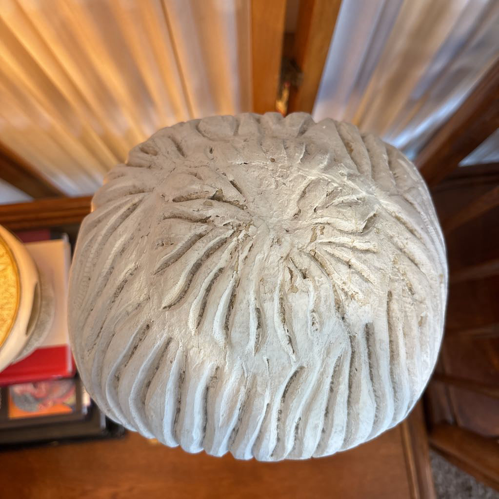 A round, ribbed concrete planter pot shown from a top-down perspective on a wooden surface with curtains in the background.