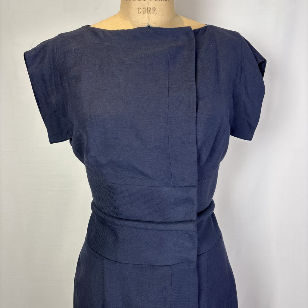A navy blue short-sleeve dress displayed on a mannequin torso against a plain light background. The dress features a unique wrap-style front panel and a matching waist belt.