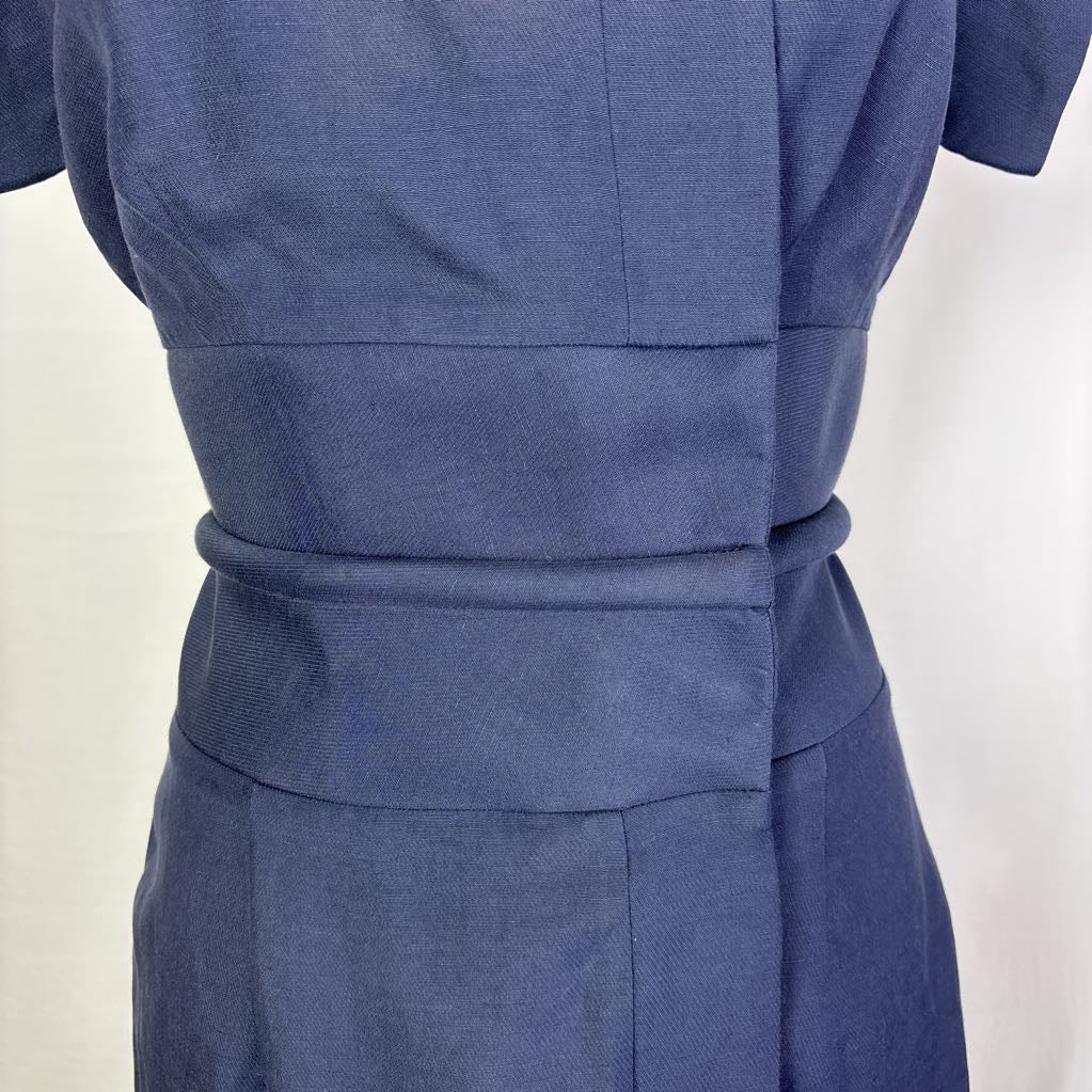 Close-up of the back waist of a blue short-sleeve dress with a matching fabric belt, shown on a mannequin against a plain light background.