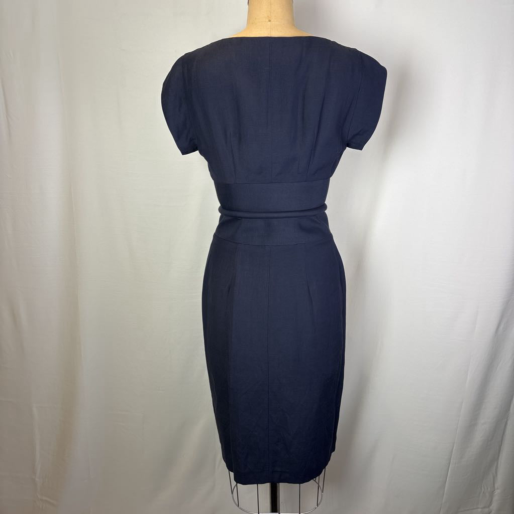 A navy blue short-sleeve knee-length dress displayed on a mannequin from the back, set against a white fabric backdrop.