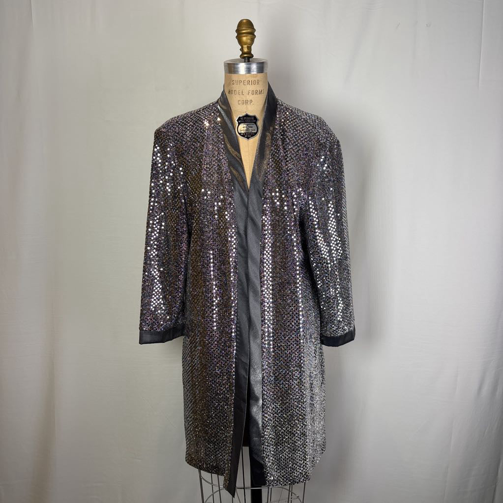 A black and silver sequined open-front jacket with three-quarter sleeves, displayed on a dress form mannequin against a white fabric backdrop.