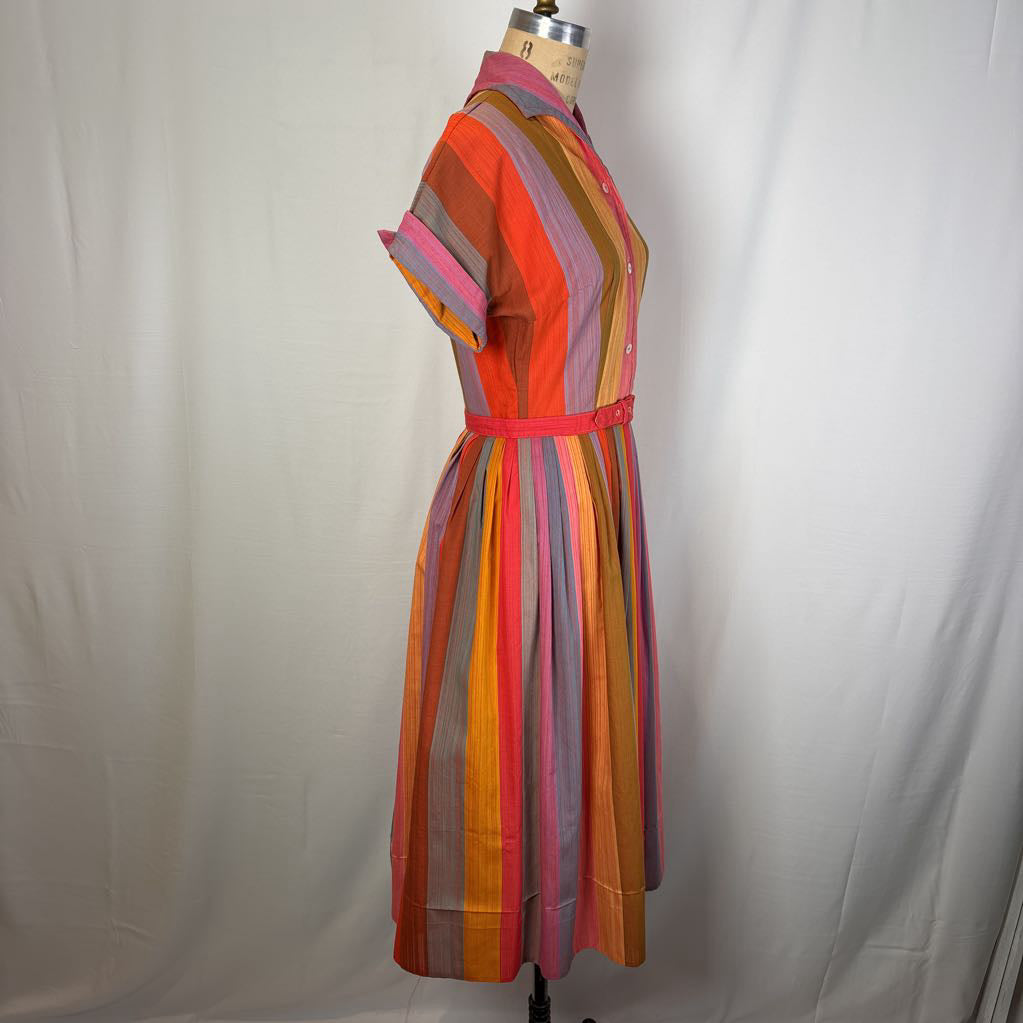 A short-sleeve collared dress displayed on a dress form against a white fabric backdrop. The dress features vertical stripes in orange, pink, yellow, purple, and gray, with a matching pink waist belt.