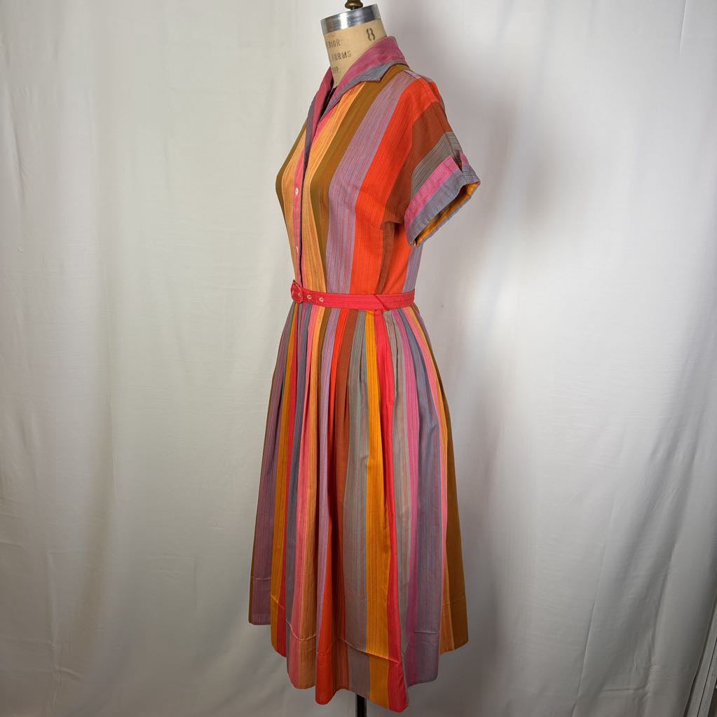 A short-sleeve collared dress with vertical multicolor stripes in orange, pink, yellow, purple, and brown, displayed on a dress form against a white fabric backdrop.