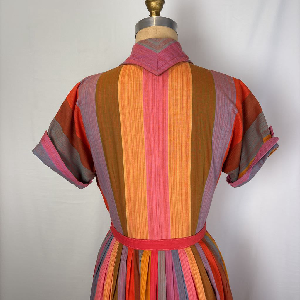 A short-sleeve collared dress shown from the back on a dress form, featuring bold vertical stripes in orange, pink, brown, red, and gray with a matching waist belt.