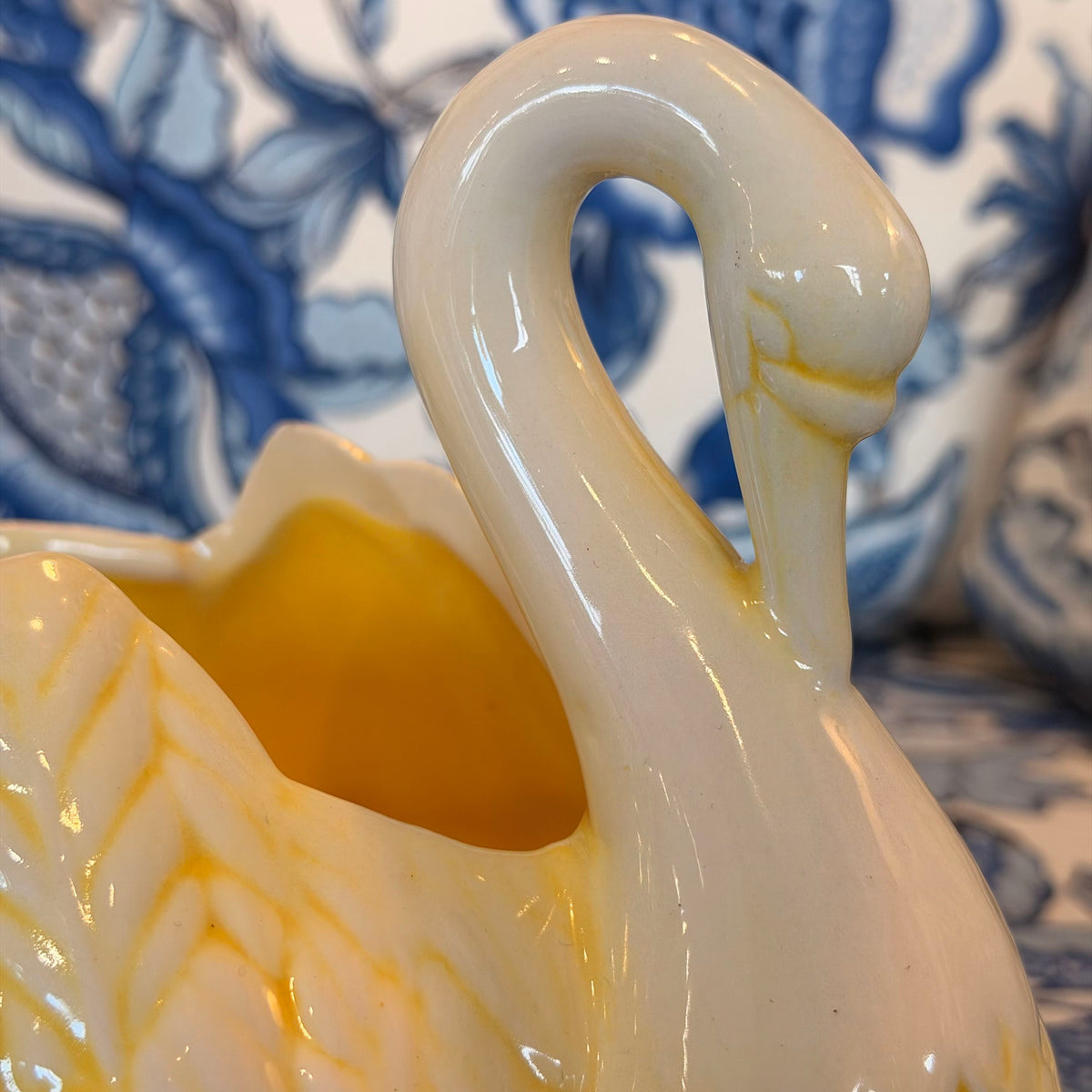A yellow and cream-colored ceramic swan figure on a blue and white fabric surface.