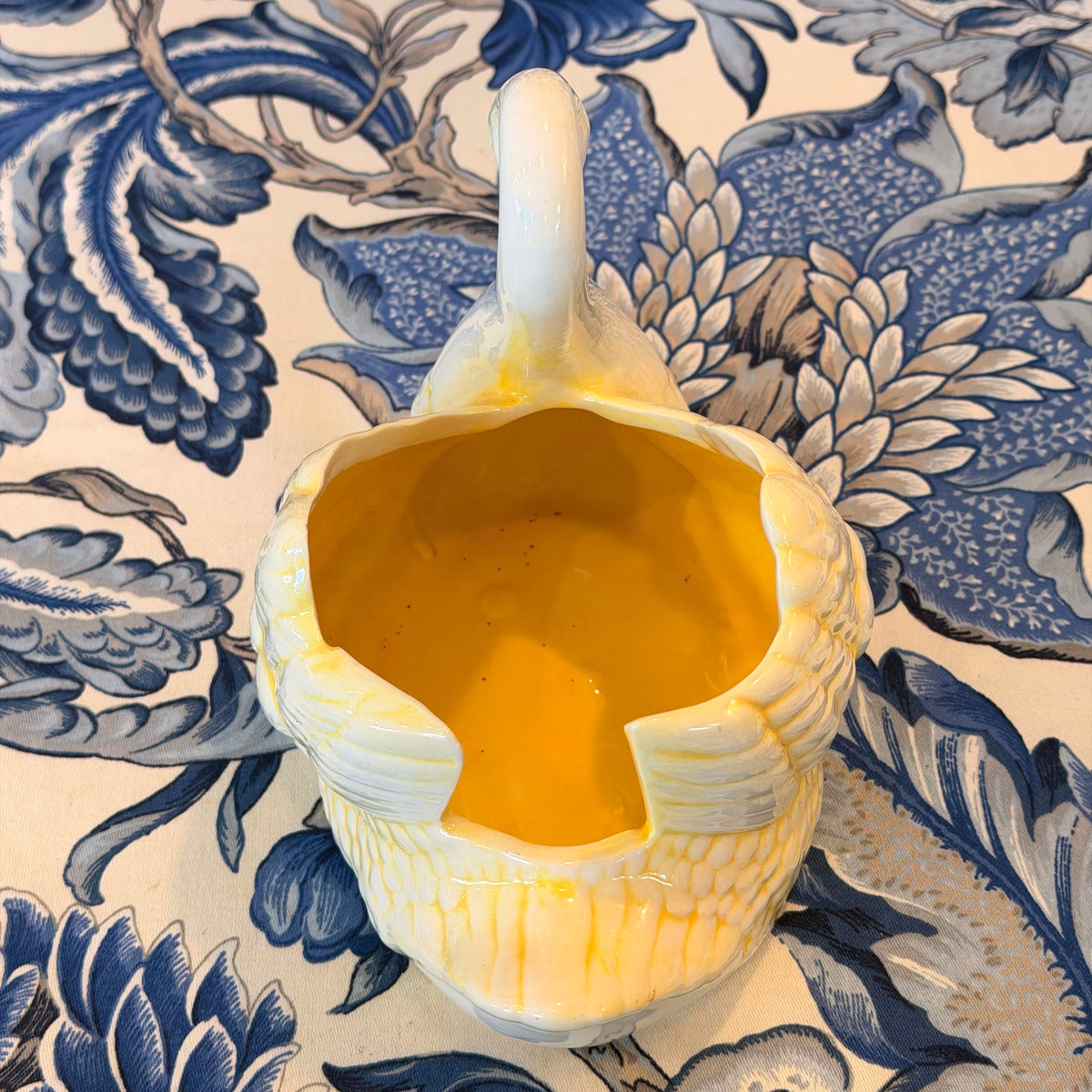A yellow and cream-colored ceramic swan figure on a blue and white fabric surface.