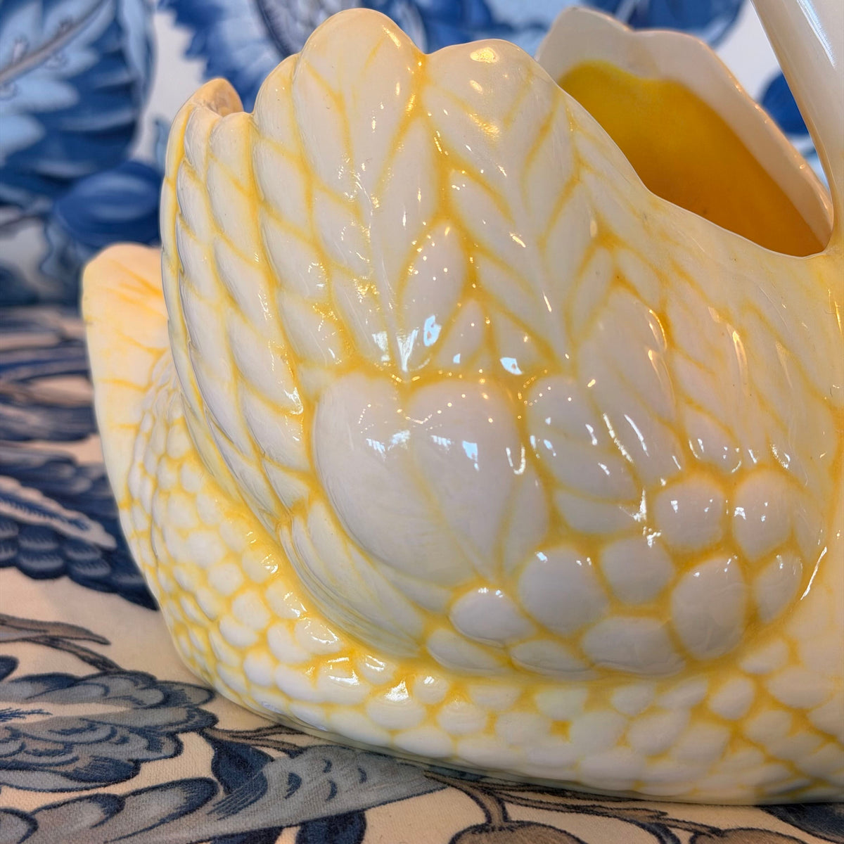 A yellow and cream-colored ceramic swan figure on a blue and white fabric surface.