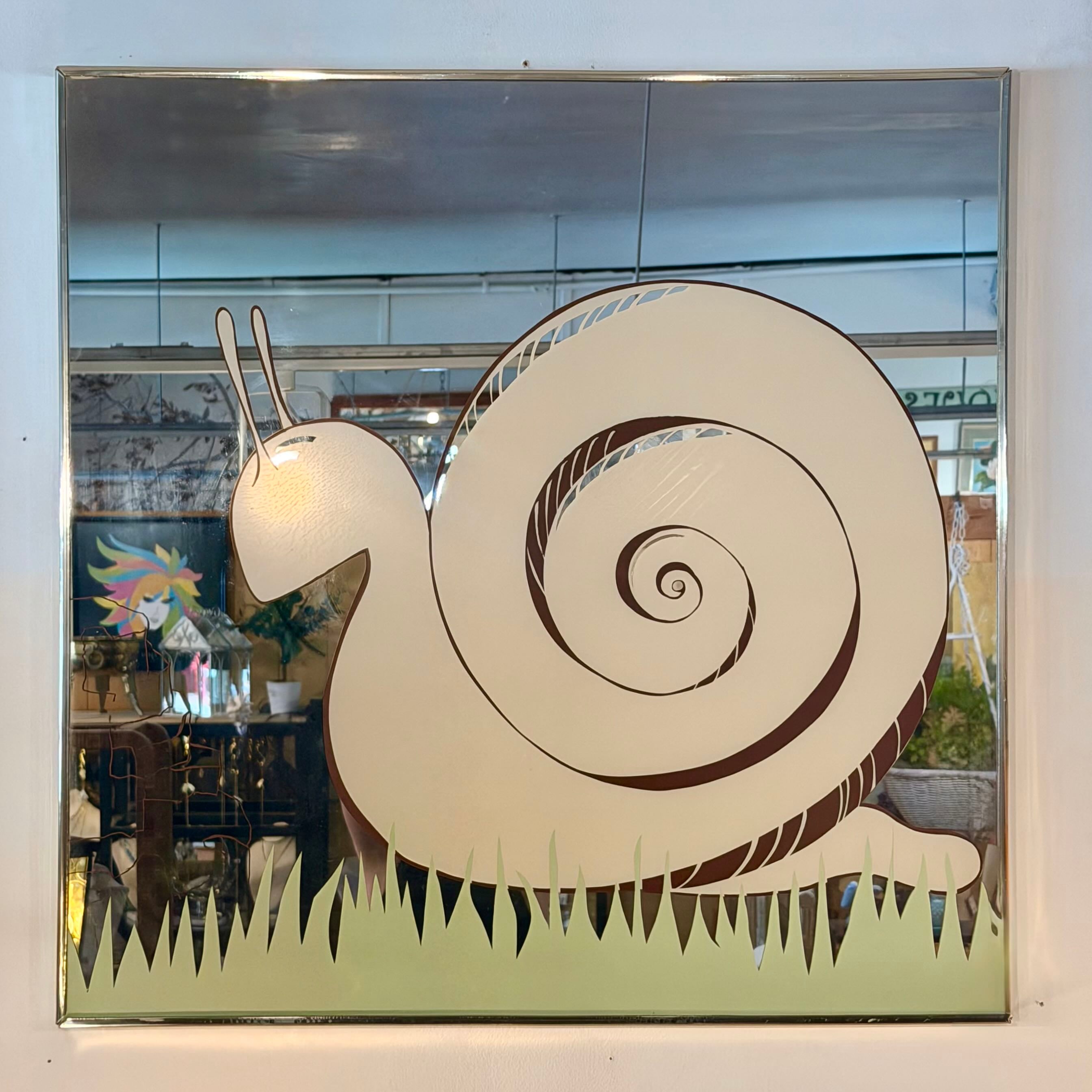A square decorative mirror with a stylized snail design etched or painted across the reflective surface, shown hanging on a wall with indoor reflections visible behind it.