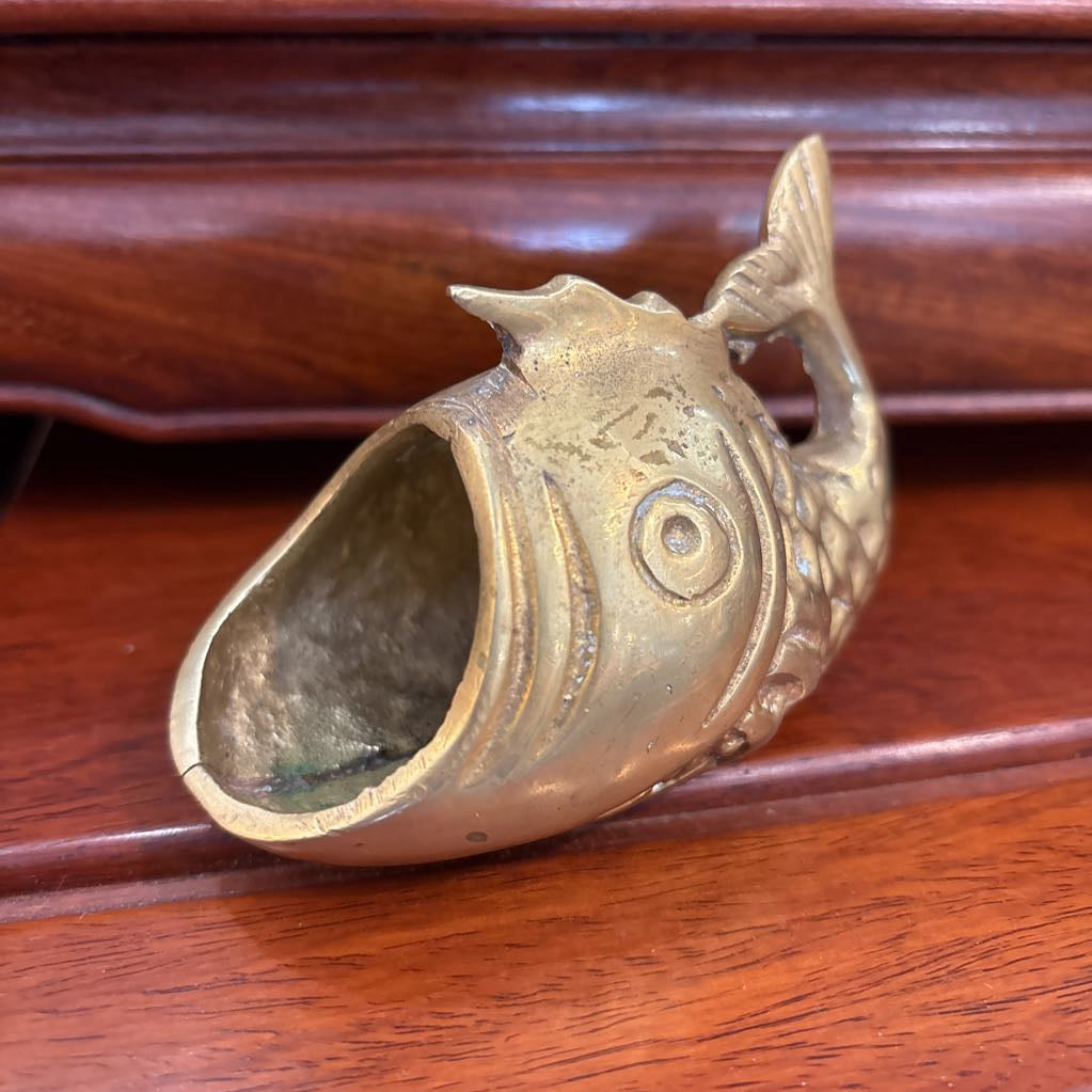 A brass fish figure with its mouth wide open on a brown wooden surface.