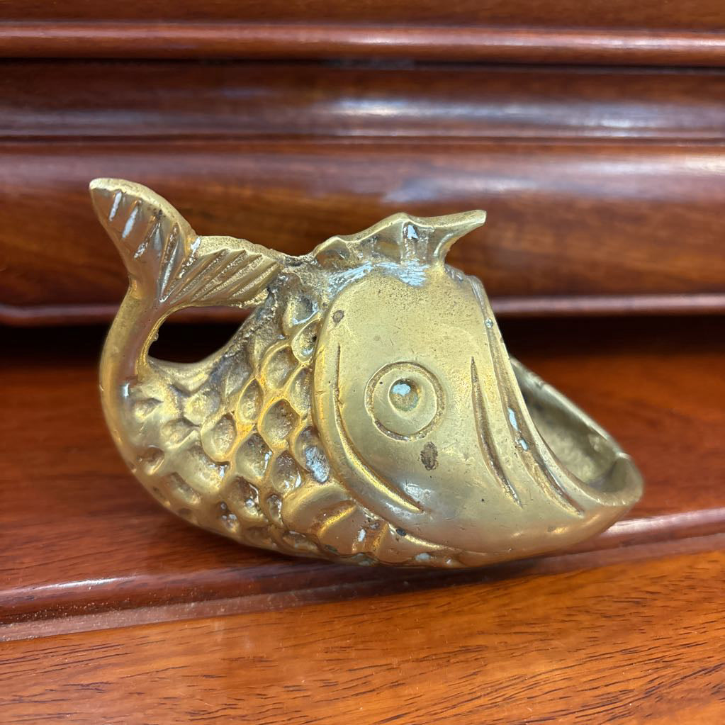A brass fish figure with its mouth wide open on a brown wooden surface.