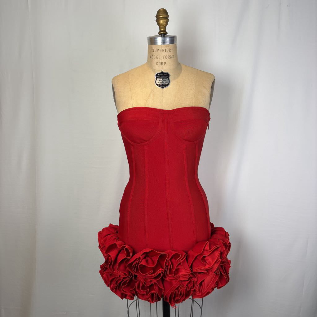 A bright red strapless corset-style dress displayed on a dress form mannequin against a plain light gray fabric backdrop.