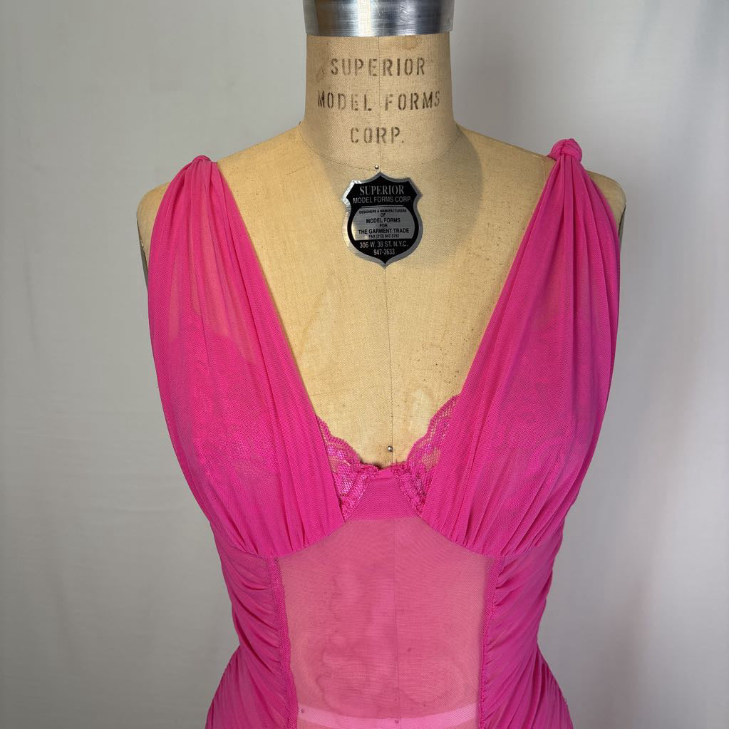 A bright pink vintage lingerie dress displayed on a tan mannequin torso. The garment features a deep V-neckline with sheer mesh panels and lace trim, with a vintage 'Superior Model Forms Corp.