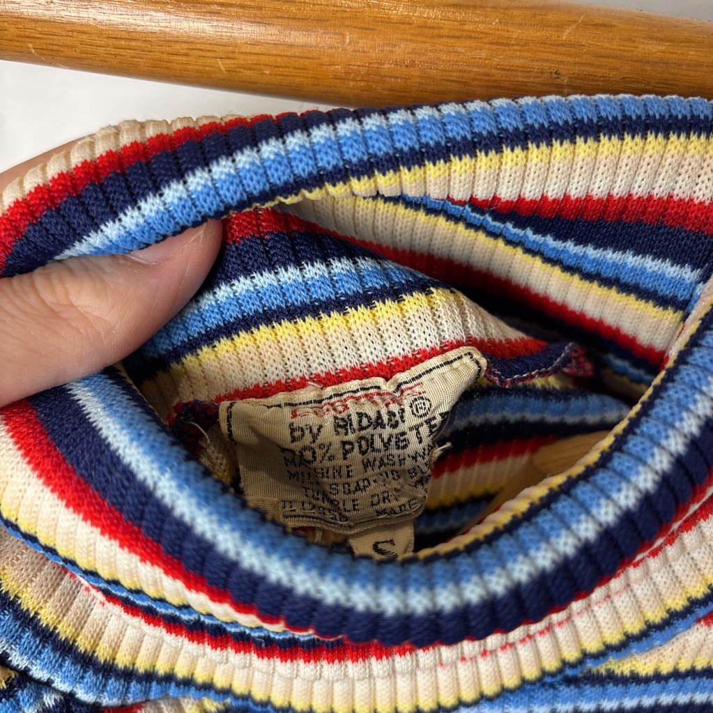 A hand holding open a striped turtleneck sweater showing a brand tag on the inside.