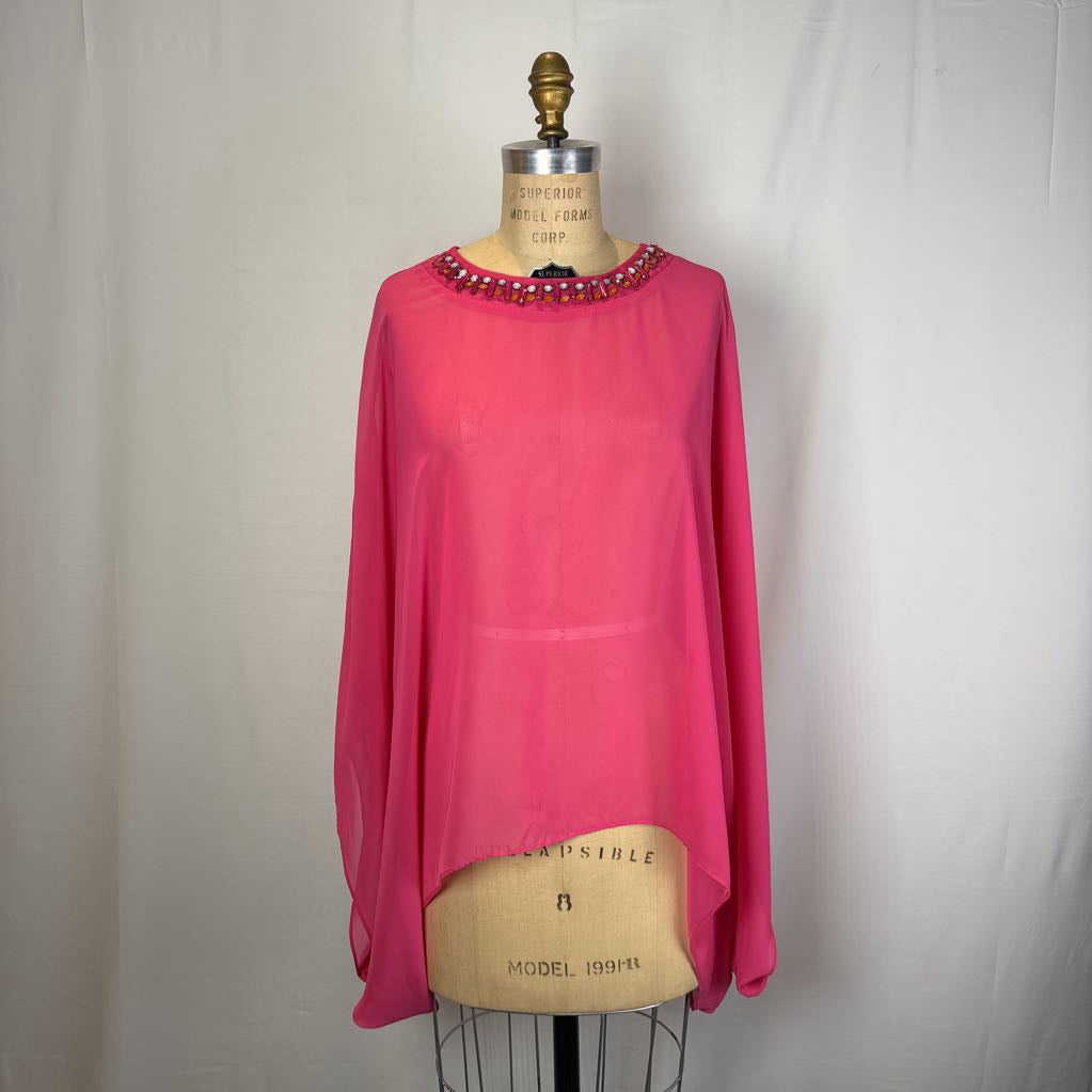 A bright pink high-low blouse with a beaded neckline, displayed on a vintage burlap dress form mannequin against a white fabric backdrop.