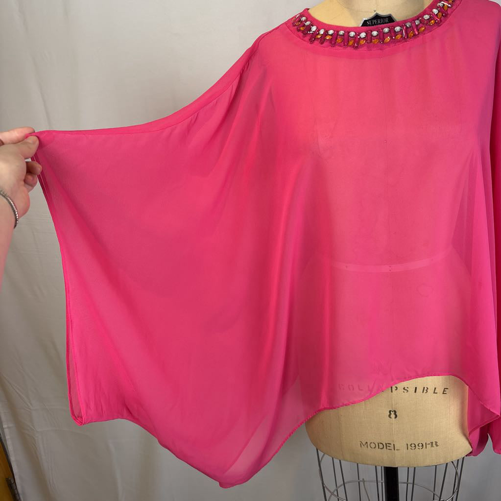A bright pink sheer blouse with a beaded neckline, displayed on a dress form with a hand holding the left sleeve out to show the flow, against a neutral fabric backdrop.