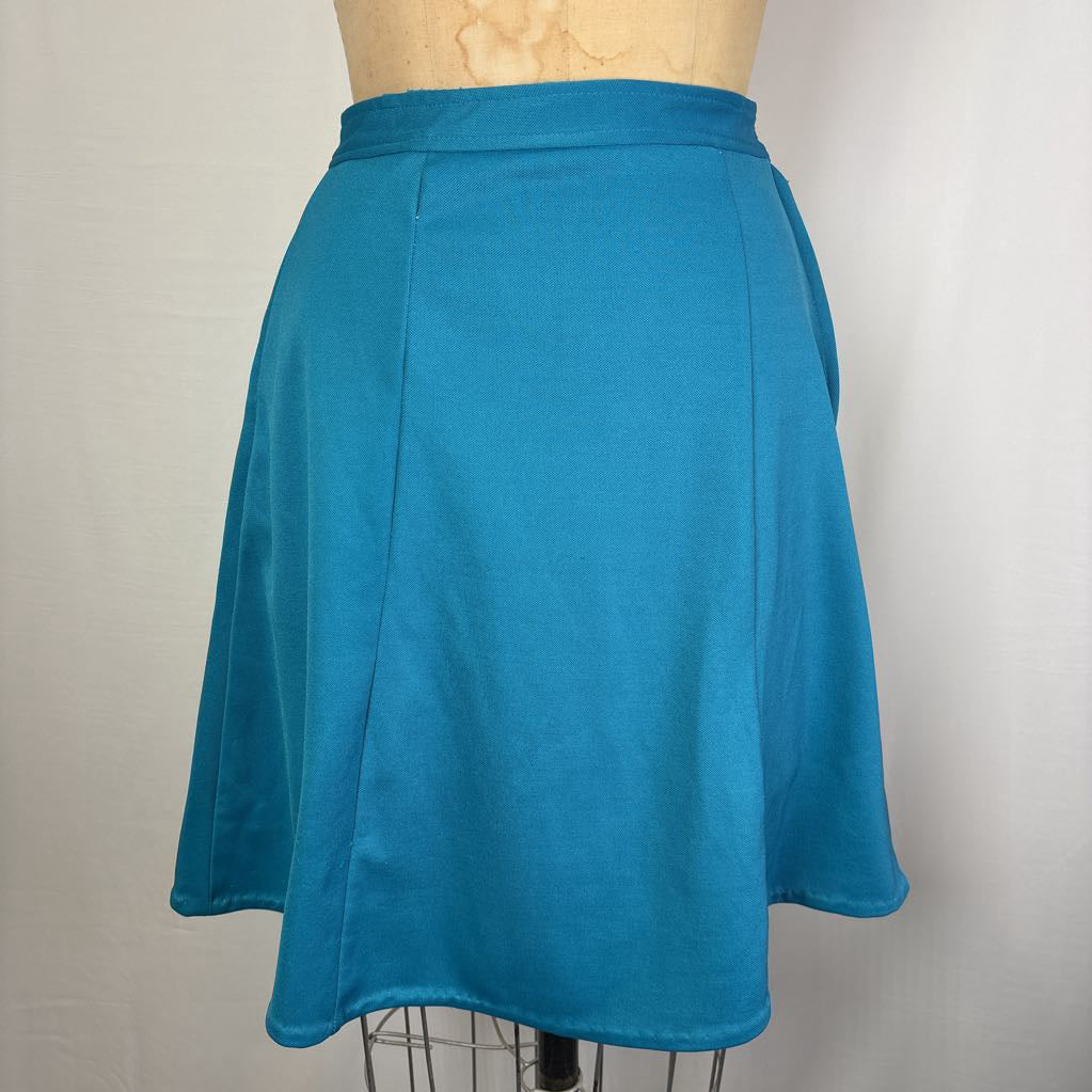 A bright teal blue A-line skirt displayed on a dress form mannequin against a light gray fabric backdrop.