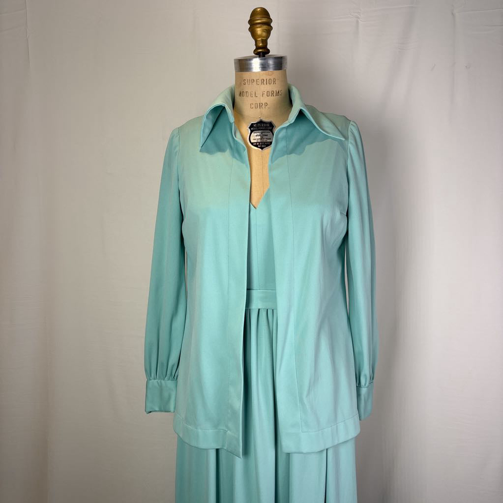 A mint green two-piece set consisting of a long-sleeve collared button-up shirt and matching skirt, displayed on a vintage dress form mannequin against a white fabric backdrop.