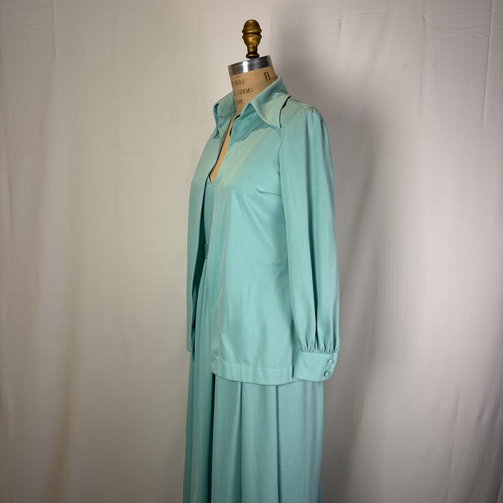 A mint green two-piece set consisting of a long-sleeve collared button-up shirt and matching pleated skirt, displayed on a dress form mannequin against a white fabric backdrop.